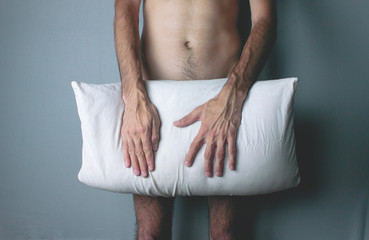 A young naked man covers his penis with a pillow.