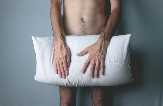 A young naked man covers his penis with a pillow. Stock-foto | Adobe Stock