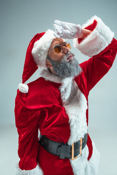Funny serious guy with christmas hat posing at studio. New Year Holiday. Christmas, x-mas, winter, gifts concept. Man wearing Santa Claus costume on gray. Copy space. Winter sales.
