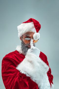 Funny serious guy with christmas hat posing at studio. New Year Holiday. Christmas, x-mas, winter, gifts concept. Man wearing Santa Claus costume on gray. Copy space. Winter sales.