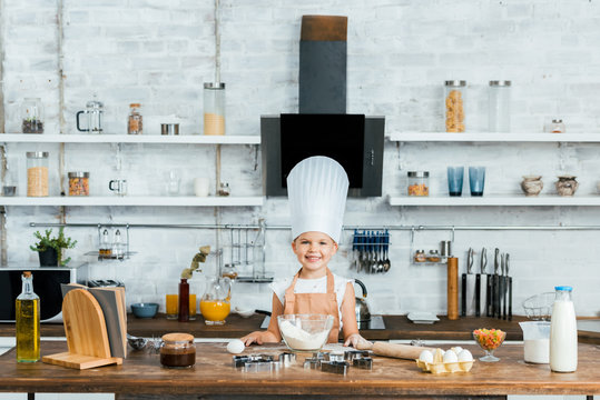adorable kid in chef hat and apron cooking dough and smiling at camera