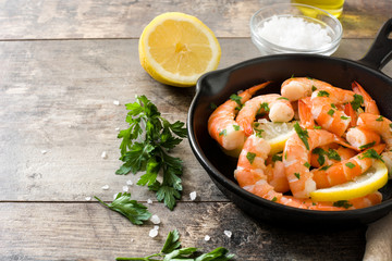 Grilled shrimps, parsley and lemon in iron pan on wooden table. Copyspace