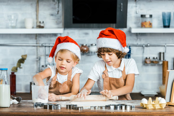 adorable chldren in santa hats and aprons preparing christmas cookies together
