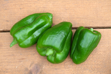 Still life with three appetizing whole green ripe bell peppers on brown wooden  surface tom view close up