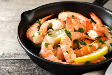 Grilled shrimps, parsley and lemon in iron pan on wooden table