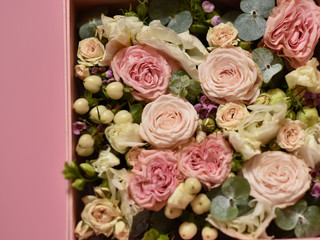 bouquet of small pink and peach roses with greens in a gift box on a pink background