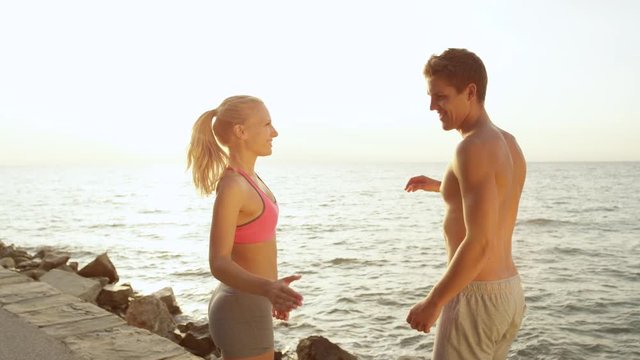SLOW MOTION, CLOSE UP: Happy training partners shake hands after a fun summer workout by the calm sea. Caucasian boyfriend and girlfriend celebrate finishing a jog by the picturesque summer seaside.
