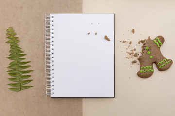 Ginger bread cookies on craft background. Blank notepad with leaf of fern. Christmas mockup. Top view.