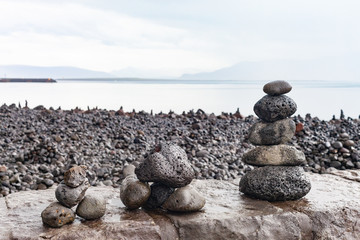 Cairns in the rain built by tourists on the shoreline of Faxafloi Bay near the Harpa Concert Hall and Conference Centre in Reykjavik, Iceland.