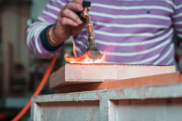 Artisan and carpenter burning wood planks, focus on the gas burner pistol, made of brass and orange...