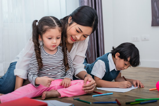 Mother teaching children in drawing class. Daughter and son painting with colorful crayon color in home. Teacher training students in art classroom. Education and Learning development of kids theme.