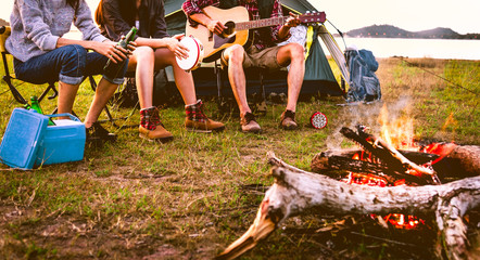 Travelers camping doing picnic and playing music in meadow field. Mountain and lake background....