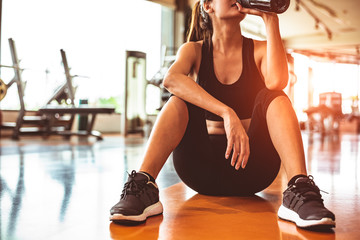 Sport woman relax resting after workout or exercise in fitness gym. Sitting and drinking protein...