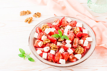 Fresh appetizer of tomatoes, feta cheese, walnuts, flax seeds and sesame seeds in a plate on a wooden table