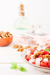 Fresh appetizer of tomatoes, feta cheese, walnuts, flax seeds and sesame seeds in a plate on a white wooden table