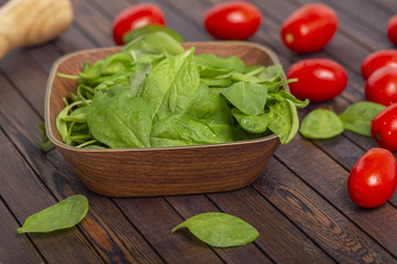 Tomatoes and spinach leaves on wooden table