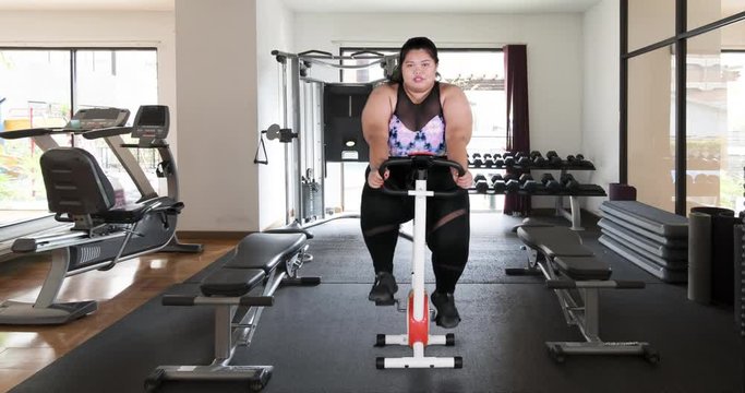 Overweight young woman in sportswear cycling in gym. Shot in 4k resolution