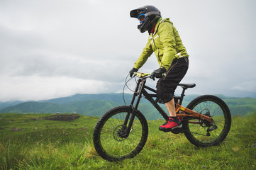 Naklejka na ściany i meble A man in a mountain helmet riding a mountain bike rides around the beautiful nature in cloudy weather. downhill