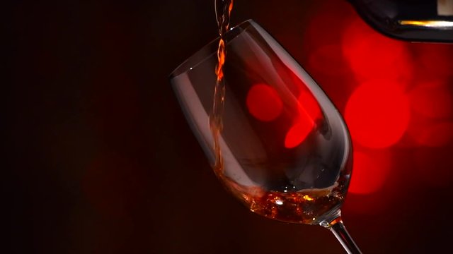 Wine. Red wine pouring in wine glass over holiday blinking background. Slow motion 4K UHD video 3840x2160