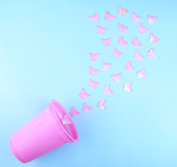 Beautiful pink artificial butterflies flying out of a pink plastic glass (on a blue paper background), minimal concept, flat lay