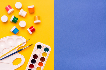 Accessories for drawing -  watercolor, gouache and brushes on a yellow-blue background. Top View....