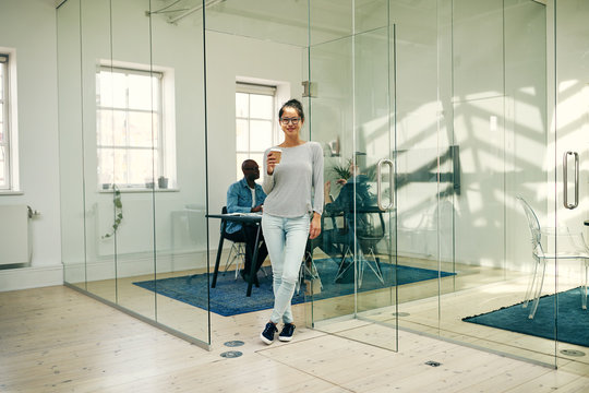 Smiling Asian businesswoman standing in an office drinking a cof
