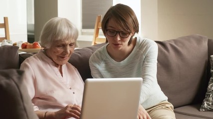 Medium shot of friendly female volunteer or granddaughter helping elderly lady and teaching her to use laptop computer - Powered by Adobe