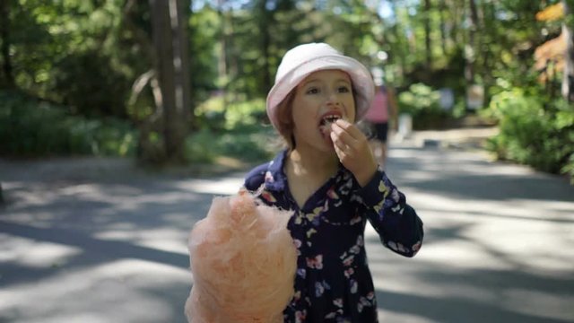 Cute little girl with pink cotton candy in the city park. Slow motion