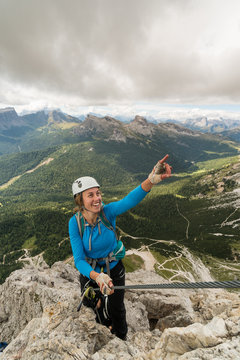 young attractive female mountain climber on a steep and exposed Via Ferrata in Alta Badia in the South Tyrol in the Italian Dolomites pointing to the summit and smiling