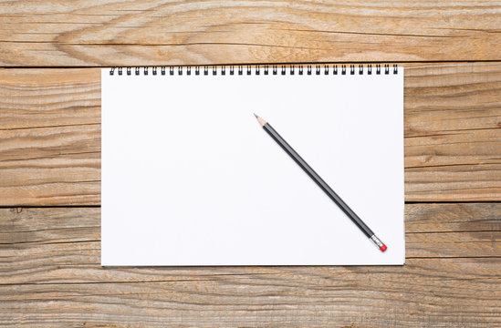 Blank page of a sketchbook with a black pencil, over old wooden texture
