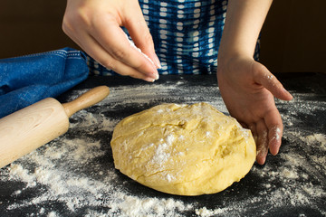 Raw dough  for baking  and women hands on the dark  background