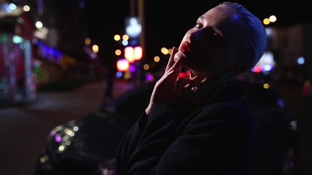 Beautiful blonde with red lips posing on camera in night city.