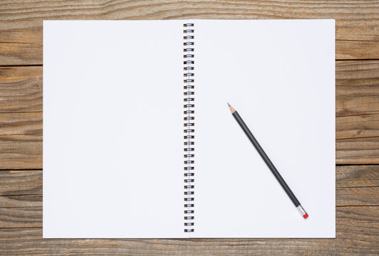 Blank page of a sketchbook with a black pencil, over old wooden texture