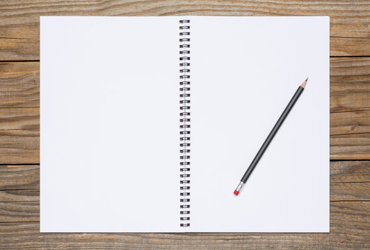 Blank page of a sketchbook with a black pencil, over old wooden texture