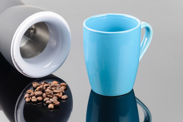 Close-up coffee grinder with coffe beans and mug on the grey mirror background. Copy space.