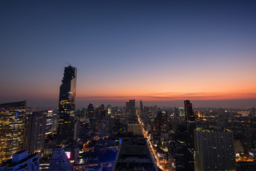 Fototapeta premium Scenic view of MahaNakhon and many other lit skyscrapers in downtown Bangkok, Thailand, from above in the evening. Copy space.