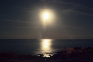 Fototapeta premium Looks like the sun but it's a long exposure of the moon over rocky cliffs and the sea. 