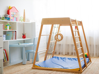 Children's room with a wooden sports complex with stairs, rings and a rope. Children's sports exercises. Physical education for children at home.