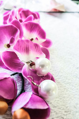 White pearl earrings handmade next to colorful flowers in a bright light. Blurred background with limited depth of field.