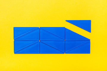 Blue plastic triangles are laid out in straight rows in a rectangle on a yellow background. Top View