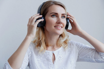 Beautiful blond girl with headphones on a light background. She enjoys listening to music and having fun.