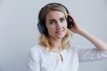 Beautiful blond girl with headphones on a light background. She enjoys listening to music, singing and having fun.