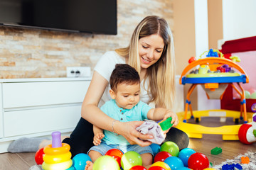 Young and happy mother playing in house with her little son