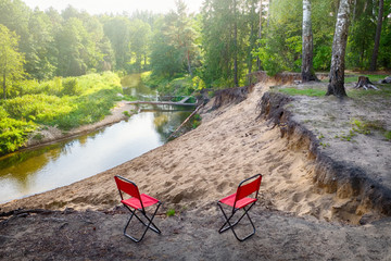 Beautiful landscape of forest river and two tourist chairs.