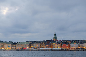 Fototapeta premium Cityscape of Gamla Stan in Stockholm, Sweden, at sunset. Old city of Stockholm at sunset during blue hour. Street lights ar on. Traces of car lamps at the foreground.