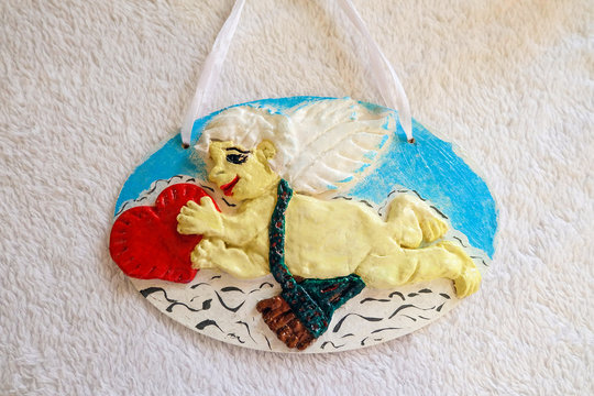 Cupid with a red heart in his hands. Handmade pendant decoration from dough.