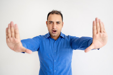Serious Indian man showing stop gesture with palms. Young guy screaming and looking at camera. Stop...
