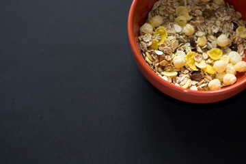 Close up muesli in ceramic red bowl isolated on black background. Heathy food, breakfast.