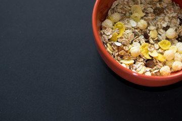 Close up muesli in ceramic red bowl isolated on black background. Heathy food, breakfast.