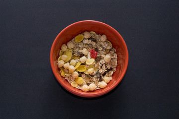 Close up muesli in ceramic red bowl isolated on black background. Heathy food, breakfast.